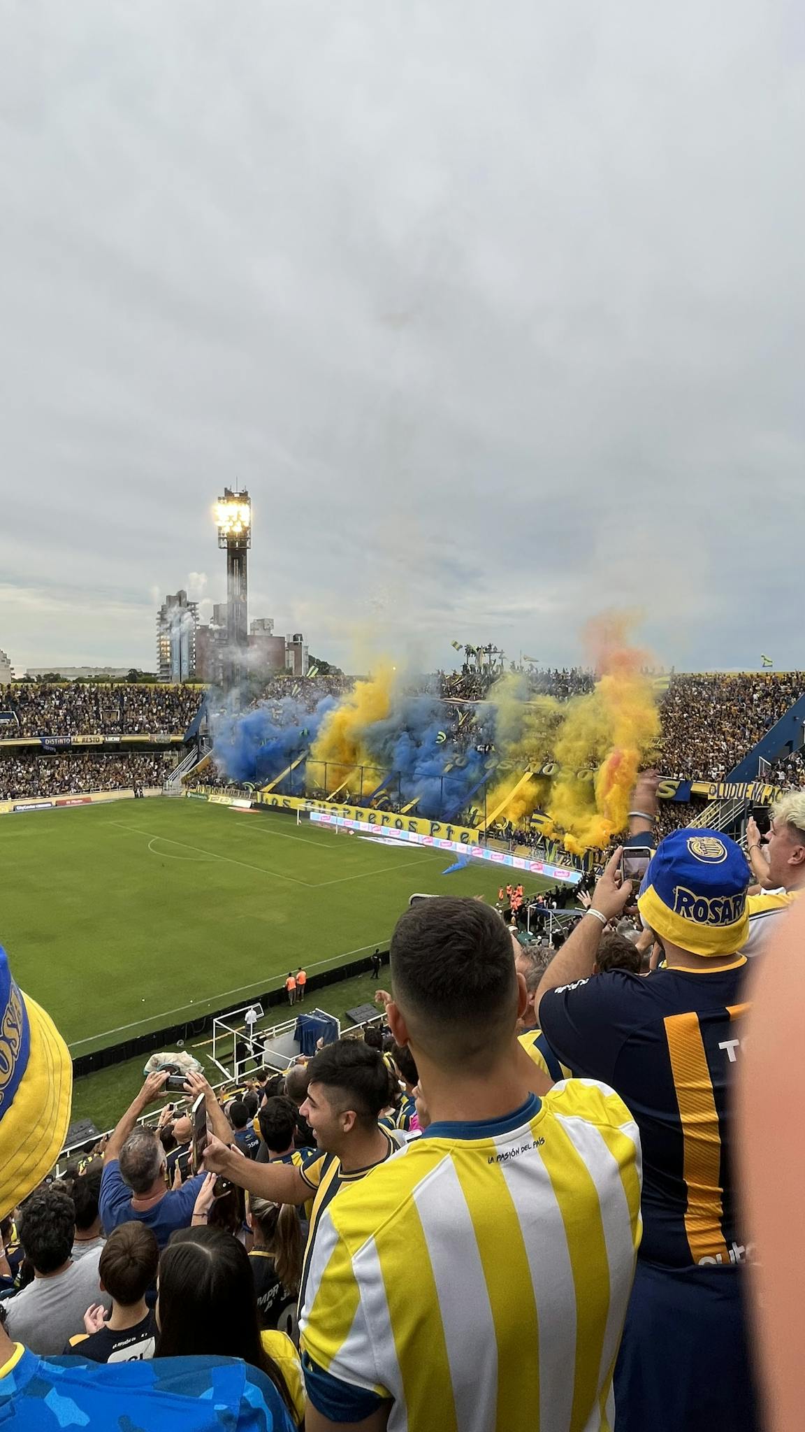 Excited fans with colorful smoke flares at a bustling football stadium.